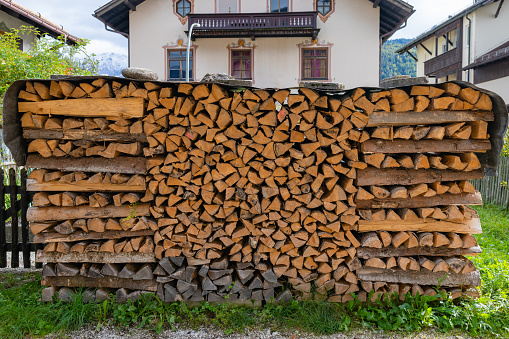 A close up of firewood stacked neatly drying outside of a residential traditional home in Garmisch in southern Germany. It is covered to prevent it getting wet as it dries out outside of a home.