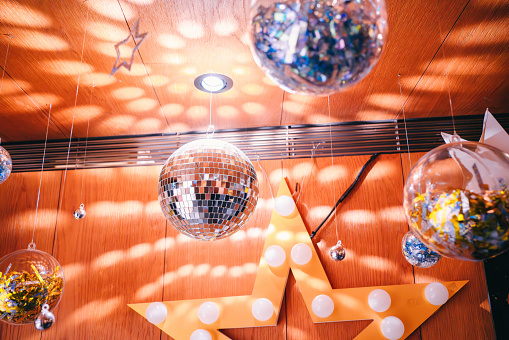 Disco ball and sparkling decorations in the retro-style room. The disco ball casts light reflections across the room, filling the space with shiny bright spot.