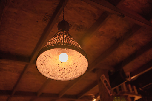 A vintage bamboo basket pendant light hanging in a wooden room.