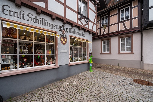 Gengenbach, Germany – August 17, 2022: A picturesque storefront located on a quaint cobblestone street with a classic clock hanging from the facade