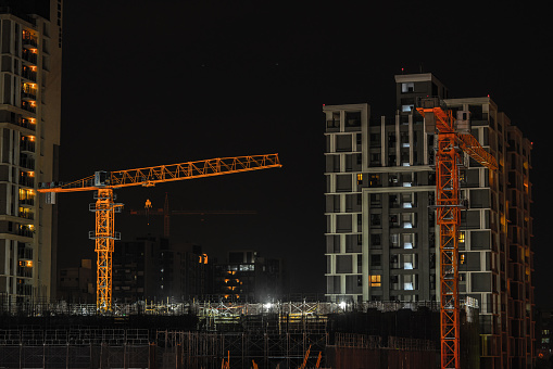Under Construction Buildings in the City at Night, with prominent orange cranes and construction site lights.
