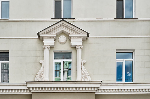 A facade of a residential building built in 1955 in the neoclassical style. A window decorated with a triangular pediment, columns, facade stucco. Architecture concept