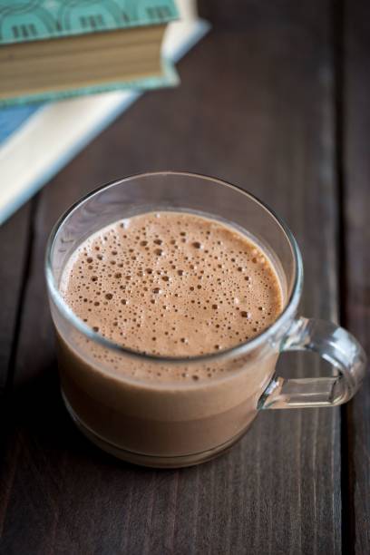 Cup of hot chocolate on a wooden table next to books.