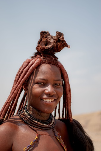 windhoek, Namibia – November 23, 2022: A portrait of a Himba tribe woman, wearing her traditional clothing and adorned with traditional jewelry, in a barren desert landscape