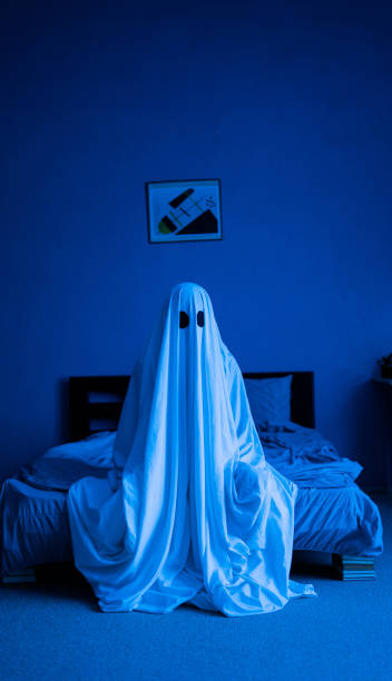 istock Ghost of Halloween sitting on the bed. Blue toned light. 1531020834