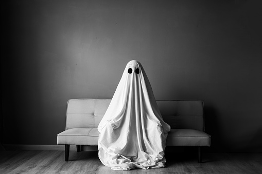 Ghost covered with a white ghost sheet on a sofa in the living room. Halloween concept. Black and white photo
