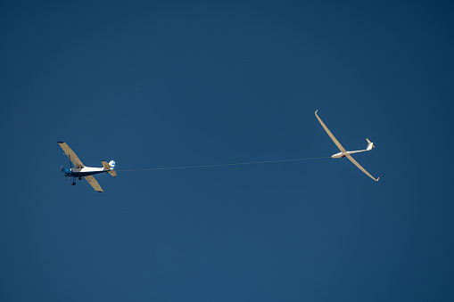 Propeller plane pulling a glider on a rope against the blue sky