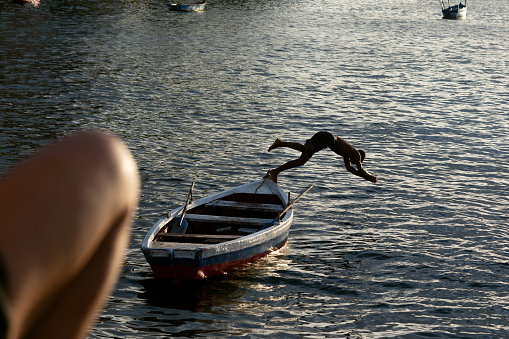 Salvador, Bahia, Brazil - January 14, 2022: Silhouette of young woman jumping from a small boat into the sea at the beach of the Museum of Modern Art in Salvador, Bahia.