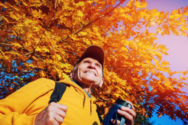 Mature alone hiker with backpack stands under bright oak tree