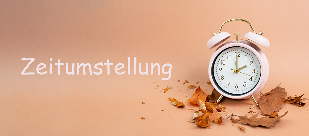 Alarm clock with autumn foliage, end of daylight saving time in fall, winter time changeover stands in german language beside the clock