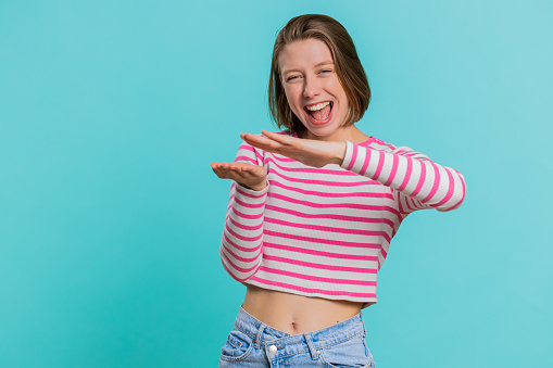 Young woman showing wasting, throwing money around, more tips, big profit, winning lottery jackpot, successful shopping payment purchase, cashback. Girl in crop top isolated on blue studio background
