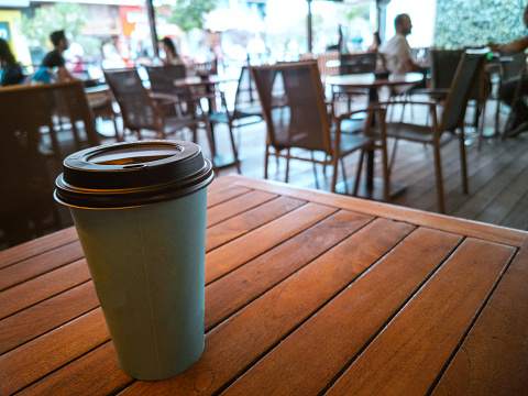 A paper coffee cup on the wooden table in a coffee shop