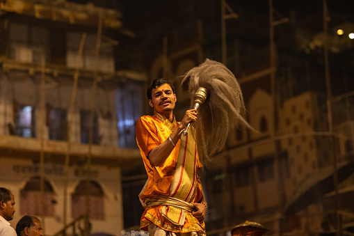 Varanasi, Uttar Pradesh, India - November 2022: Ganga aarti, portrait of hindu male priest performing holy river ganges evening aarti at dashashwamedh ghat in traditional dress with rituals.