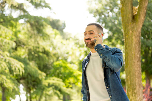 Joyful Young Man Enjoying a Stroll in the Park, Engaged in a Phone Conversation