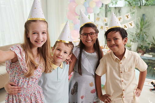 Cheerful preteen girl taking selfie with friends at birthday party