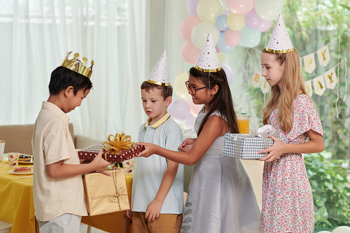 Happy kid wearing paper crown when accepting birthday presents from friends