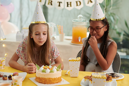 Girl in party hat blowing candle on birthday cake