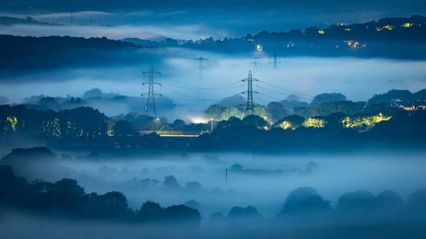 Vale enevoado à noite, mostrando postes de eletricidade - foto de acervo