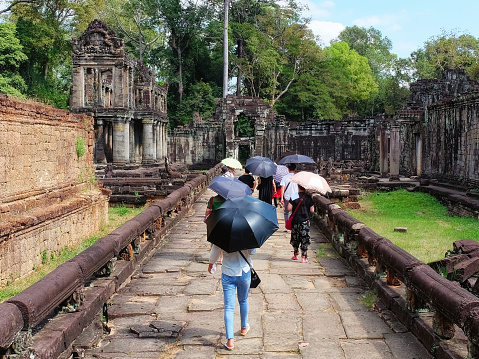 Siem Reap, Cambodia, December 19, 2018. Photograph illustrating a group of tourists using umbrellas for shade as they explore the ruins in Cambodia on a warm day.