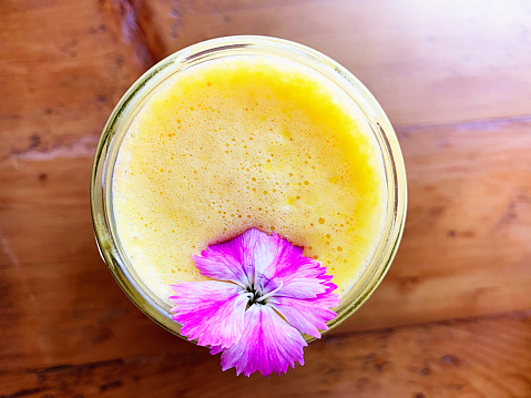 Fresh orange juice, garnished with a cute pink and white flower, on a restaurant table with rich wood grain.