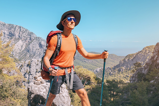 Happy hiker man with trekking backpack and hiking poles on a rocky cliff during walk on Lycian Way trail in turkish mountains