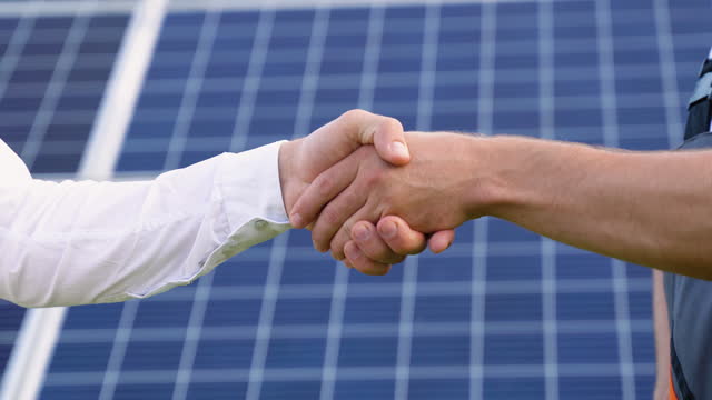 Two engineers boss and subordinate shaking hands after discussion on background of photovoltaic solar panels
