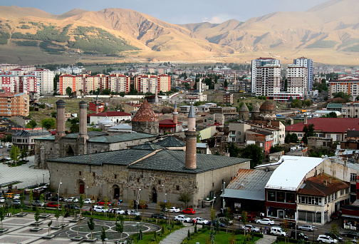Erzurum, Turkey - August 20, 2021:  Photo with the Erzurum city center with Ulu Camii mosque and Cifte Minareli Medrese against the backdrop of the sunlit mountains in Eastern Anatolia