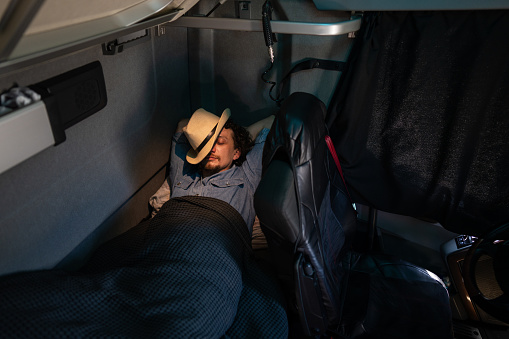 Male truck driver sleeping in passenger cabin's bed in his truck.