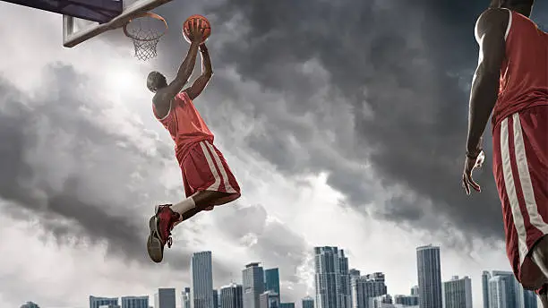 Mid air basketball player about to score, playing on outdoor city court under stormy skies with tall buildings in background