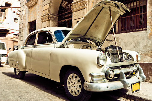 Broken retro-car with open hood parked on one of narrow streets of old Havana, Cuba