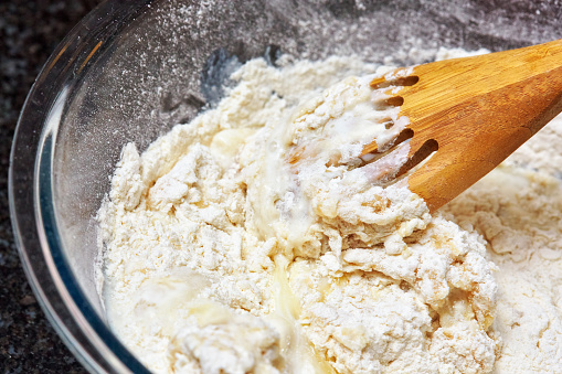 Baking ingredients in a glass bowl being mixed with wooden spoon.