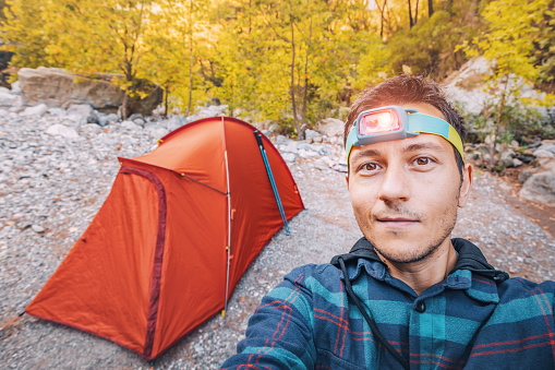 A hiker with a headlamp in the evening against the background of a tent during a trail travel
