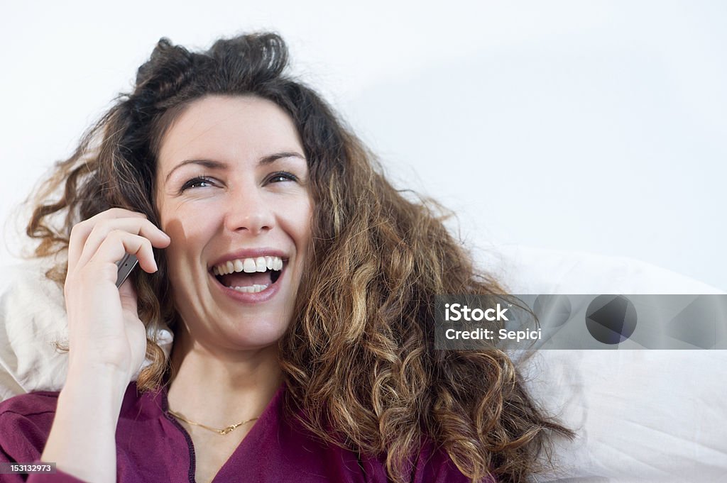 Laughing on the phone Beautiful long curly haired young woman in violet shirt cheerfully laughing while talking on her mobile phone. Possible copy space, Shallow DOF. Adult Stock Photo