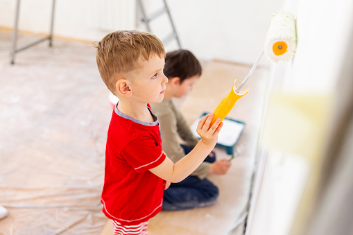 Children paint a wall with brush and roller in white color. Children paint a wall.