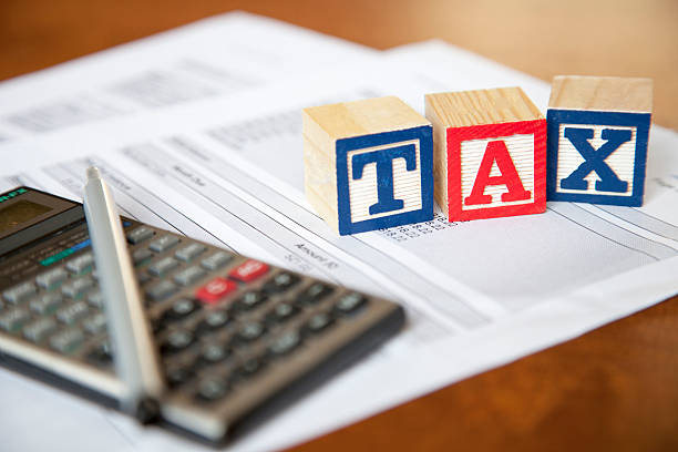 Wood blocks spell TAX on forms next to calculator stock photo