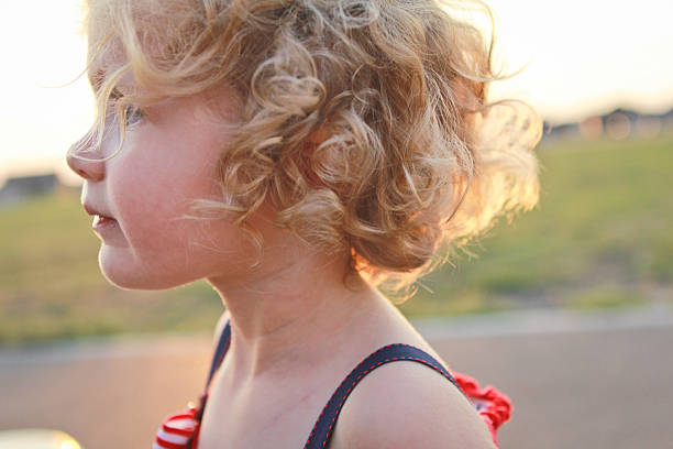 Close up profile of a 2 year old girl with curly blond hair.