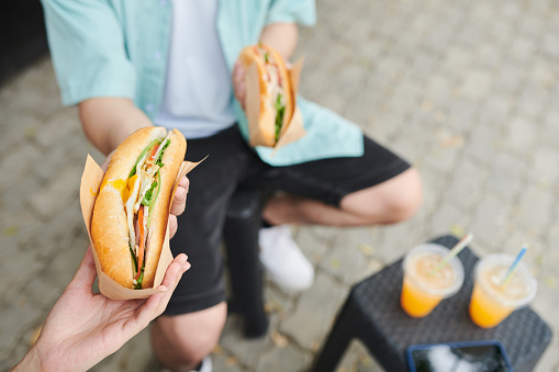 Couple eating sandwiches and drinking soda when having lunch in park