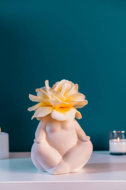 Close up white table with ceramic female body-shaped vase with rose flower, burning candles on turquoise blue wall background. Zen, cozy, meditation female bedroom decor. Self recovery place at home mesa blanca de cerca con jarrón femenino de cerámica en forma de cuerpo con flor de rosa, velas encendidas sobre fondo de pared azul turquesa. zen, acogedor, meditación decoración femenina del dormitorio. lugar de auto-recuperación en casa.