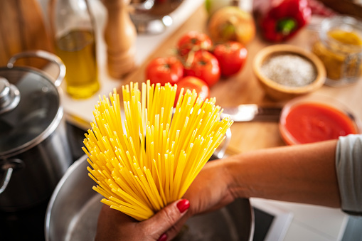 Woman holding uncooked spaghetti in a cooking pan