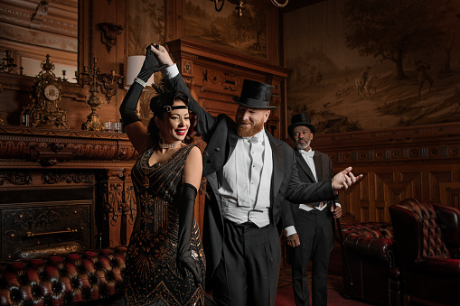 A Beautiful brunette bombshell and two handsome 1920s style white tie gentlemen in a luxury brown bar