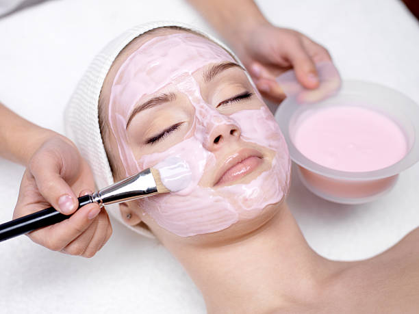 Girl receiving cosmetic pink facial mask stock photo