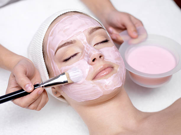 Girl receiving cosmetic pink facial mask Young beautiful girl receiving pink facial mask in spa beauty salon - indoors facial mask stock pictures, royalty-free photos & images