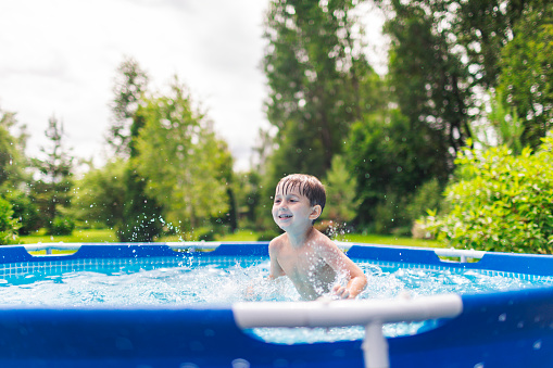 Little toddler boy having fun with splashing water in summer garden pool