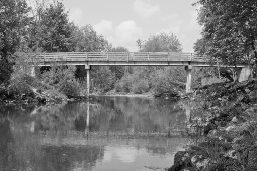 Black and white image of an old wooden bridge over calm Ljubljanica river.