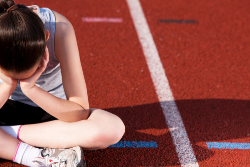 Young athlete showing disappointment. head in hands sitting crossed legged on an athletics running track. There is no eye contact. Margate Kent England April 2011