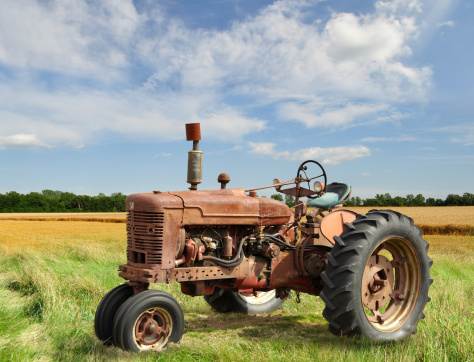A vintage red tractor on a green farm field and blue sky with cumulus clouds.
