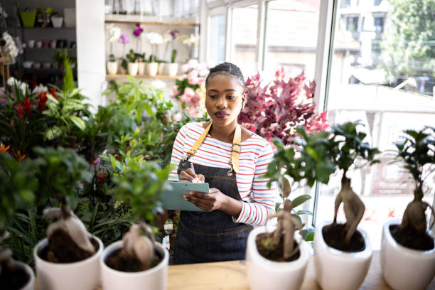 Female florist of Black ethnicity taking inventory of bonsai, at the flower shop