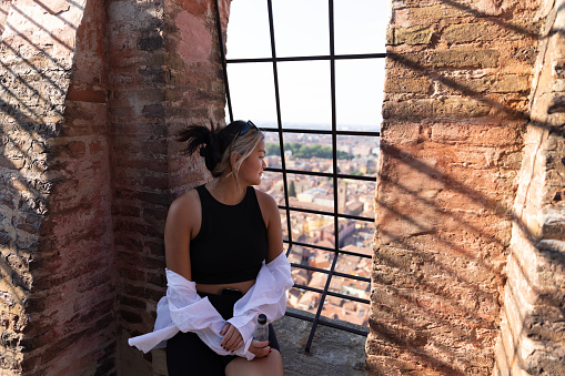 Daydreaming college student looks down on the city after climbing the stairs to the top of one of the 22 towers left in Bologna, Italy. In medieval times, Bologna had as many as 180 towers around the city.