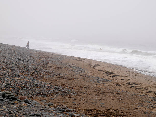 Surfista caminando por la playa en la niebla - foto de stock