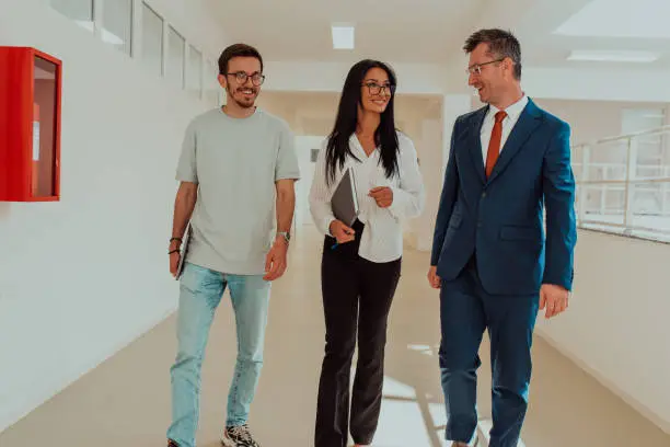 Photo of The director conducts a conversation with the secretary and a young programmer in a modern and spacious corridor of a large company, discussing various business topics and projects.